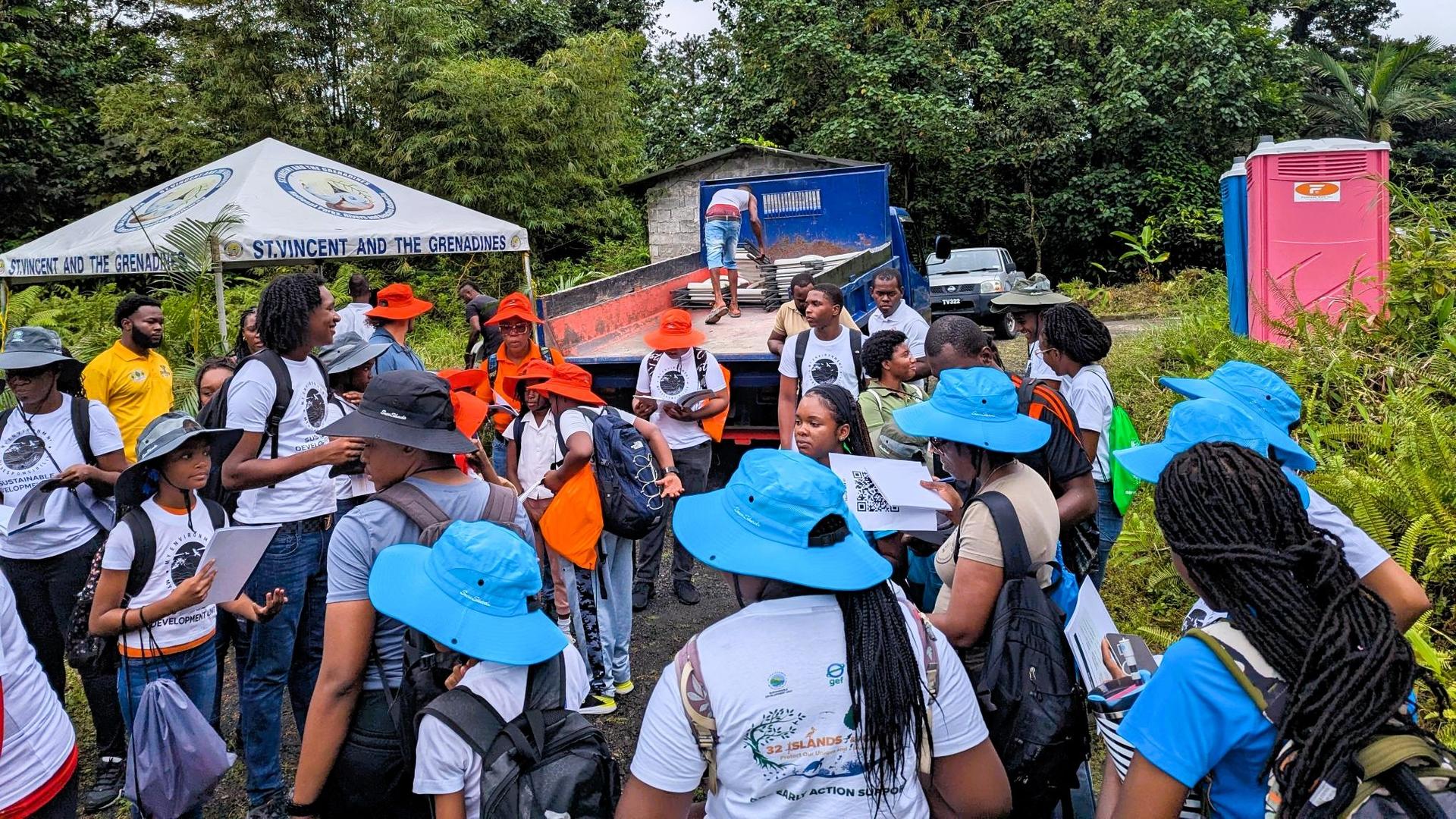 Group of people wearing blue hats gather at an outdoor event under tents and banners.