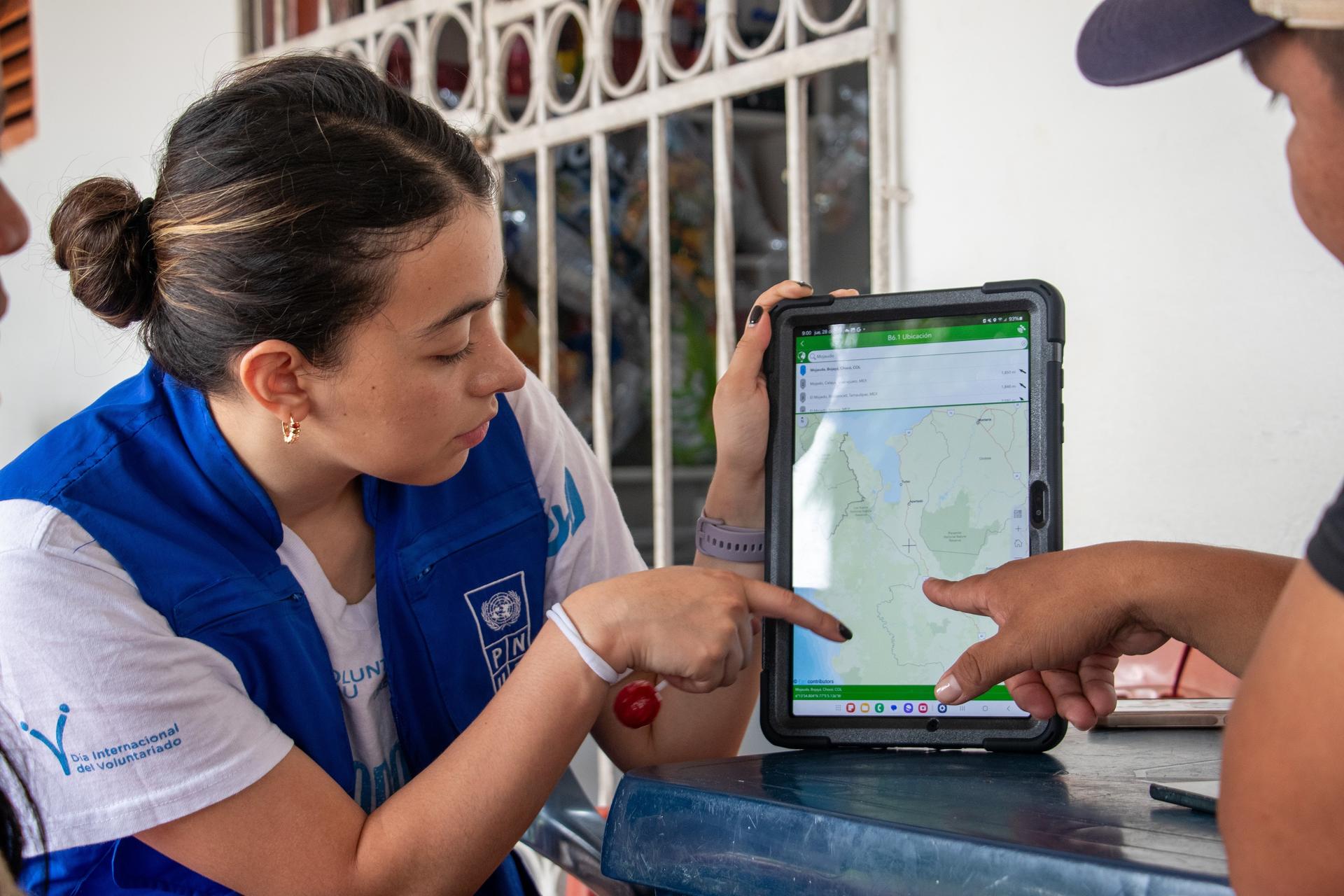 Photograph of two people using a tablet outdoors, one pointing at a map on the screen.