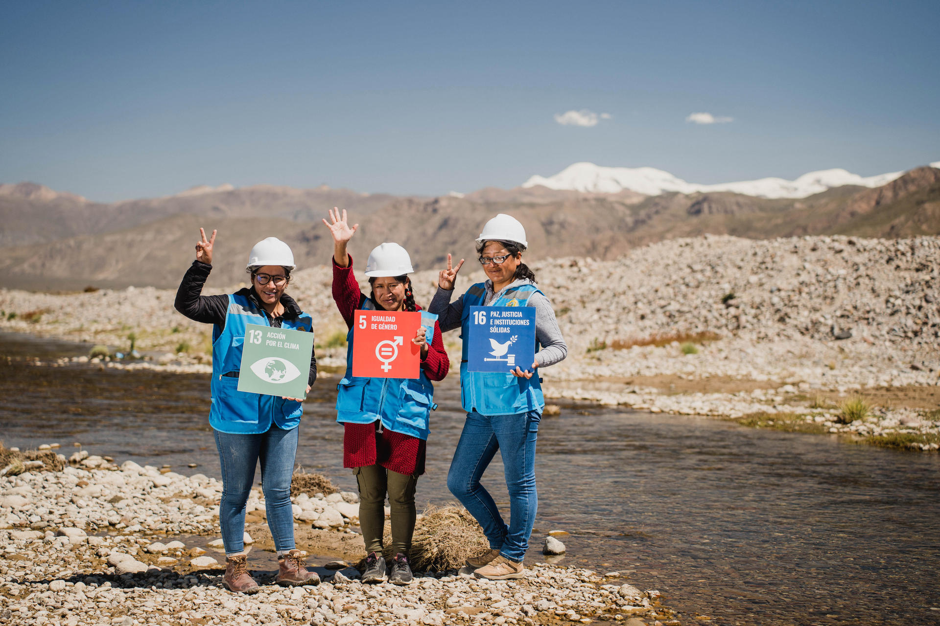 Four people in hard hats and safety vests stand on a rocky desert landscape, smiling.