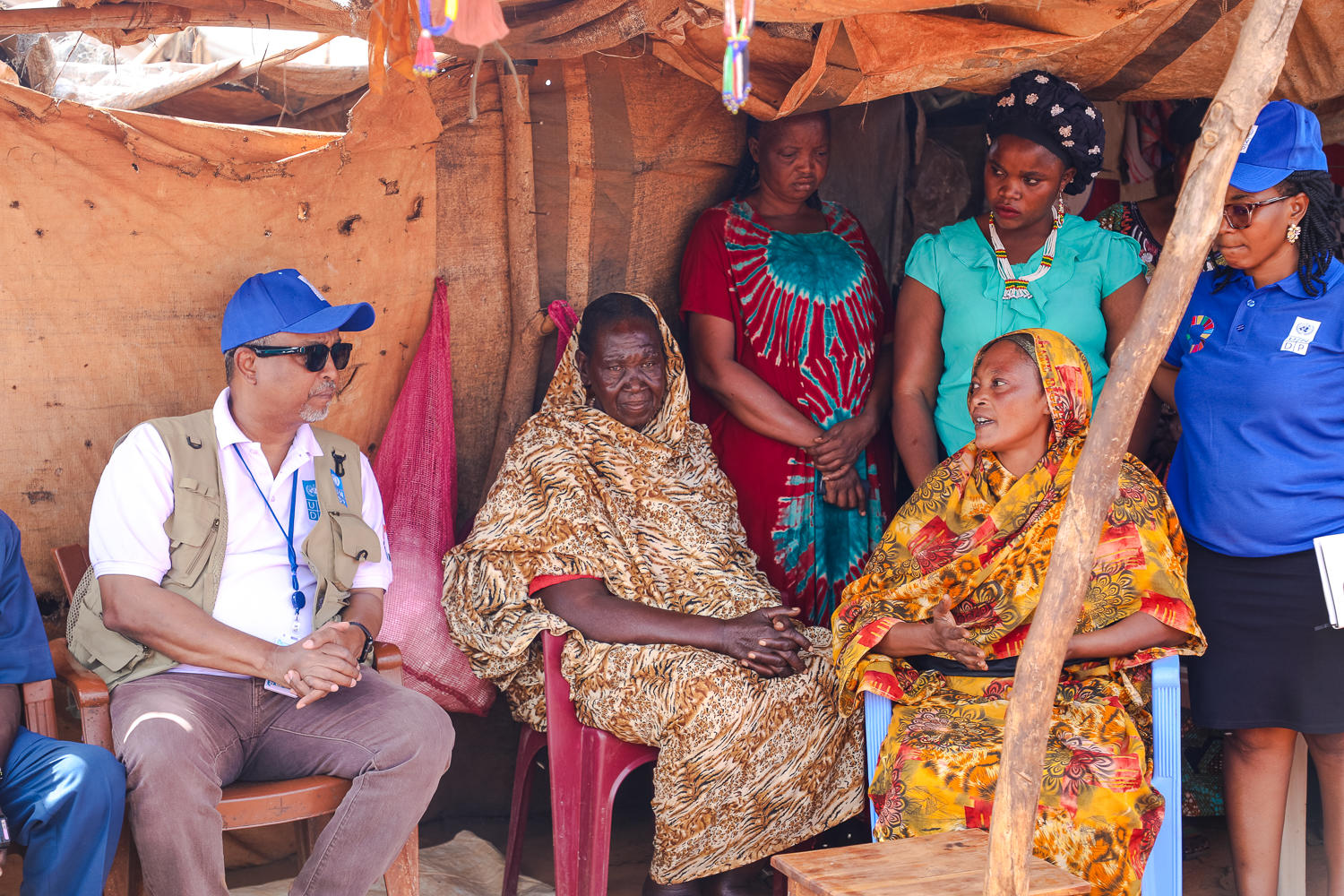 UNDP staff and local communities in a thatched shelter; women in colorful clothes.