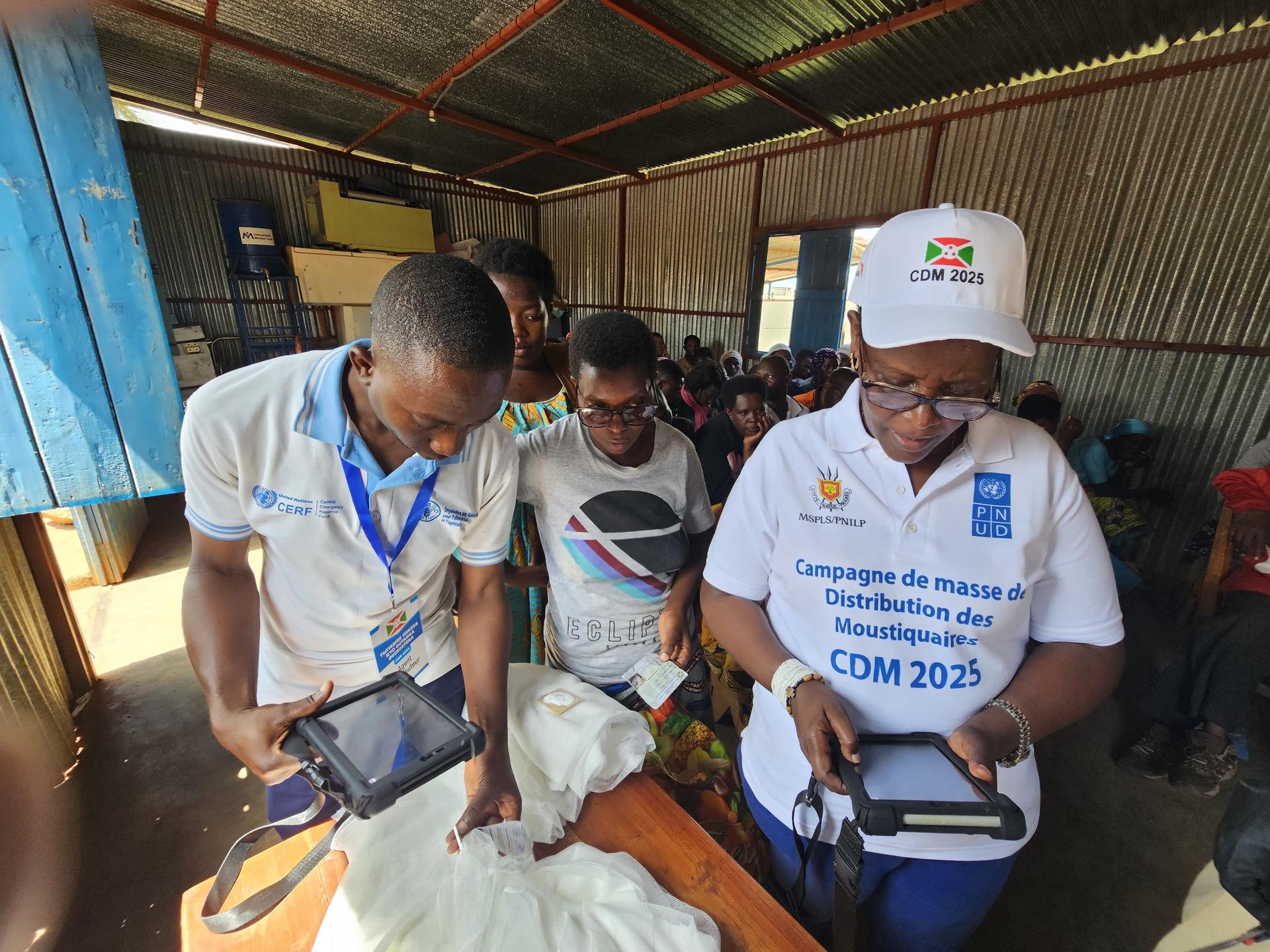 Photograph shows volunteers in white shirts assisting a patient on a bed in a shelter clinic.