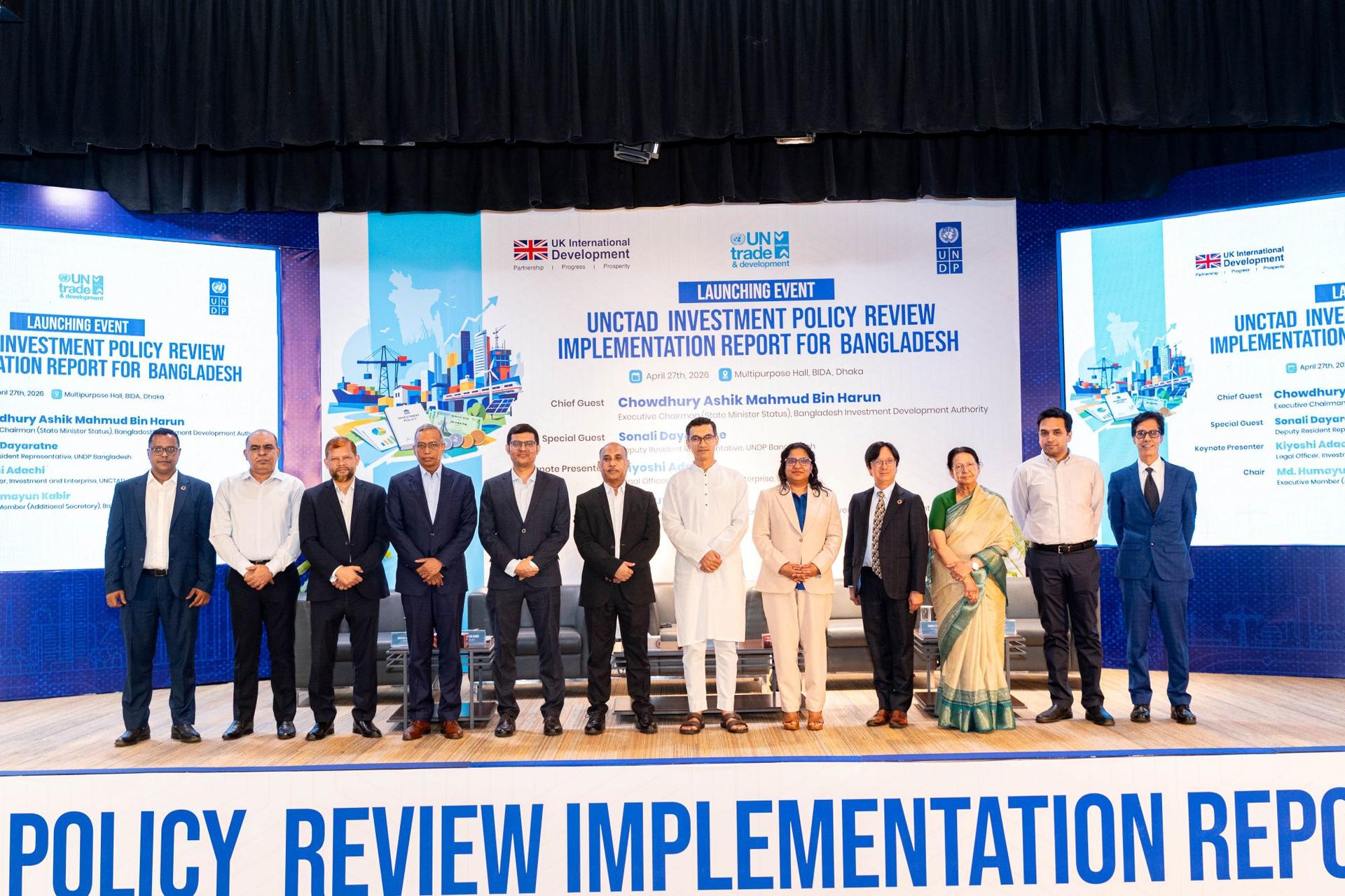 Group photo of officials on stage at a policy conference with blue banners behind.