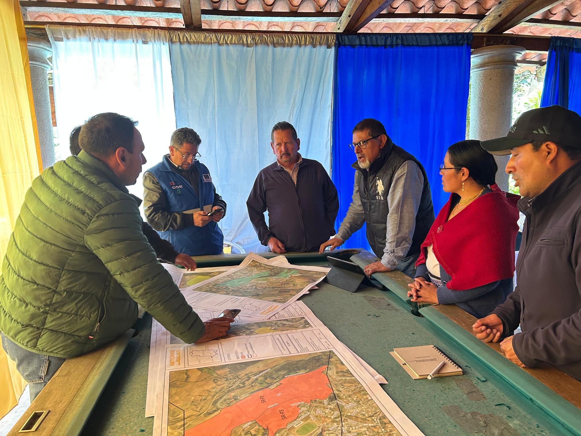 Photo: group around a table with large maps, discussing planning in a bright room.
