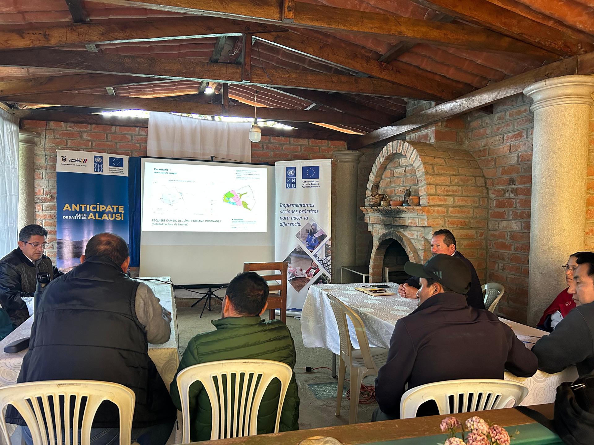 Attendees seated at tables in a rustic brick room, watching a projector presentation.