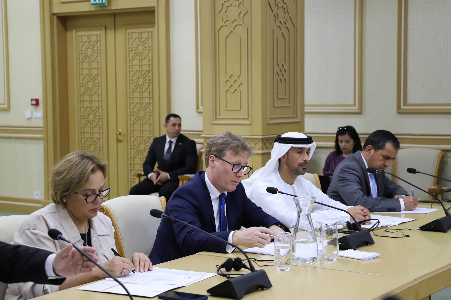 Panel of officials around a long conference table with microphones in a gold-trimmed room.