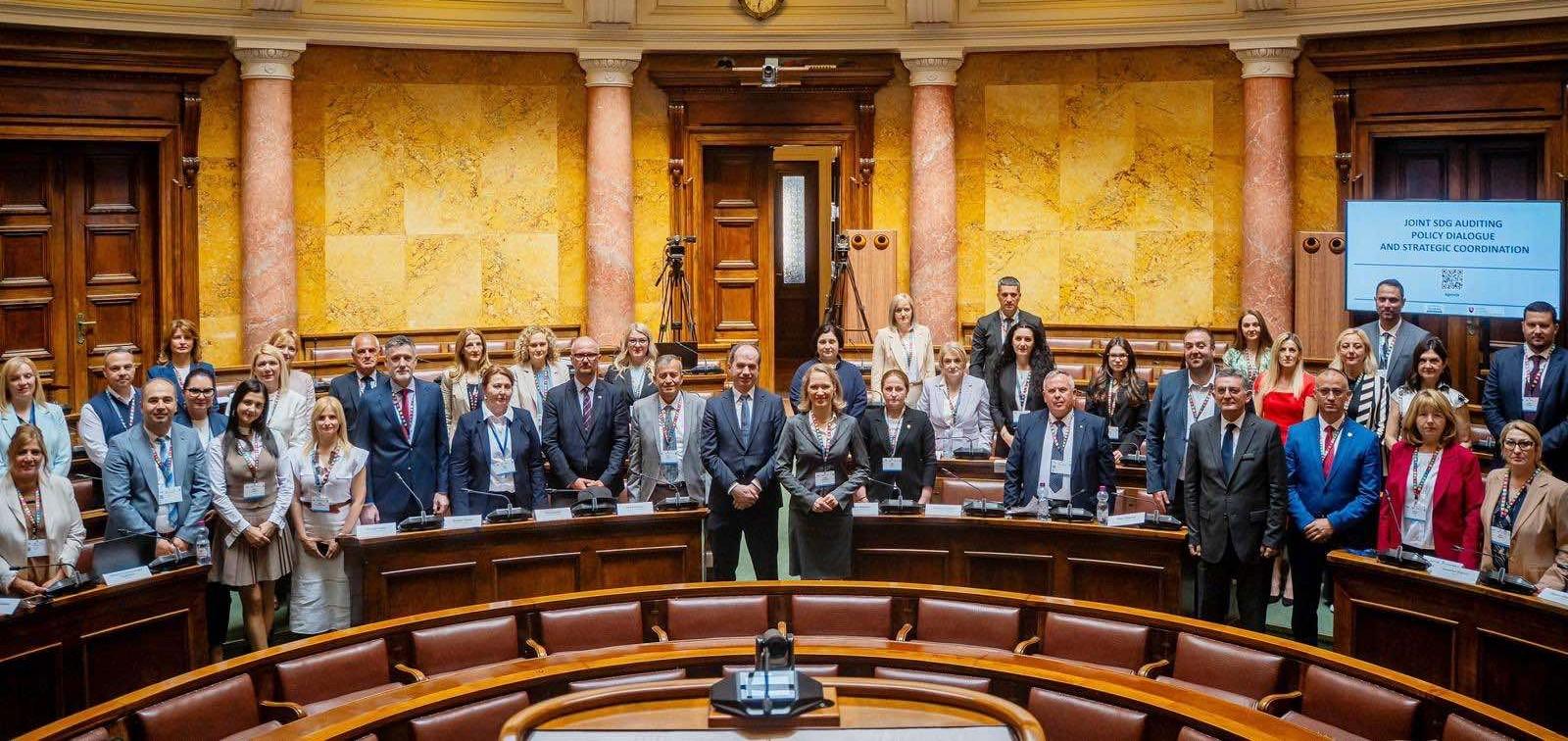 Photograph of a large group in a wood-paneled council chamber, standing in a semicircle.