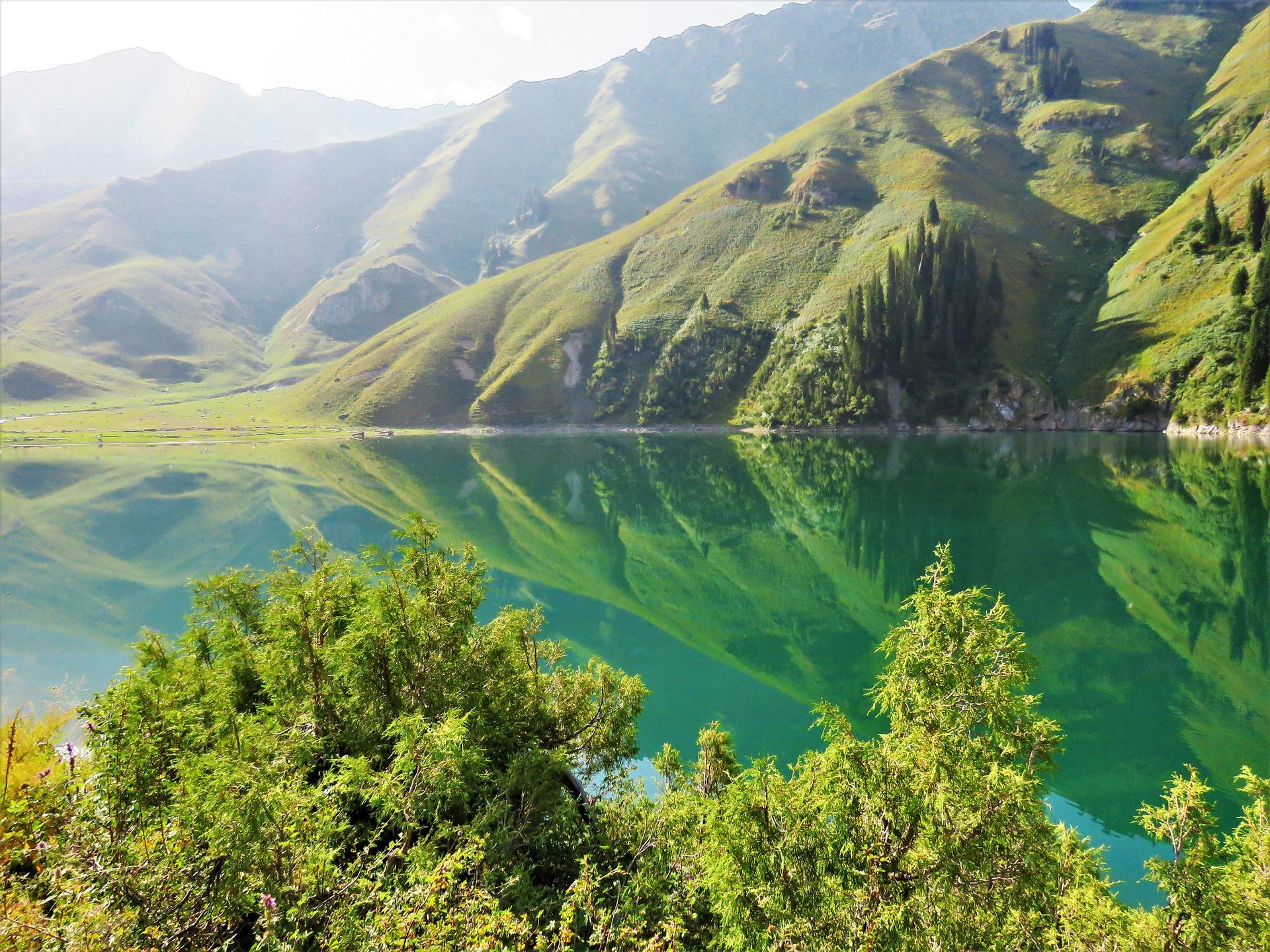Photograph of a turquoise lake framed by emerald green mountains with a leafy foreground.