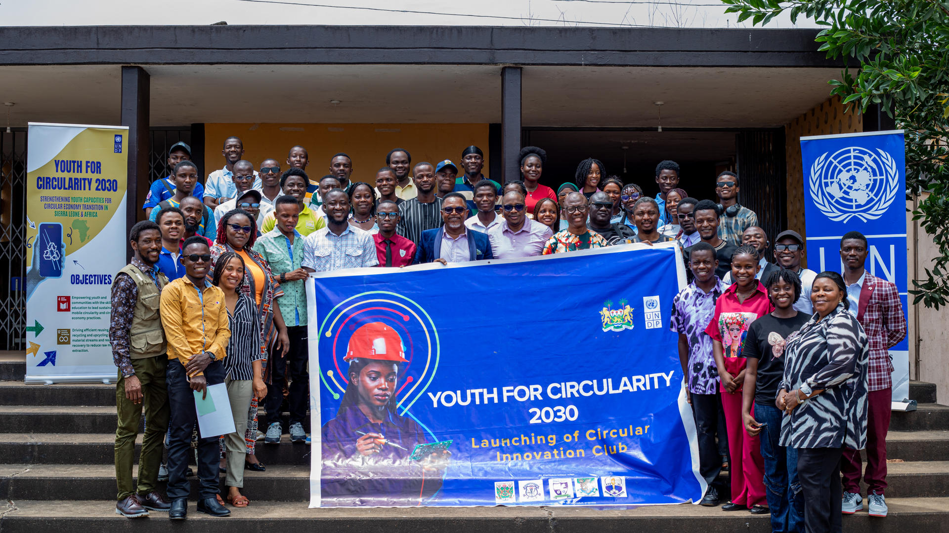 Group photo of diverse people with a blue Youth for Citizenship 2020 banner in front of a building.