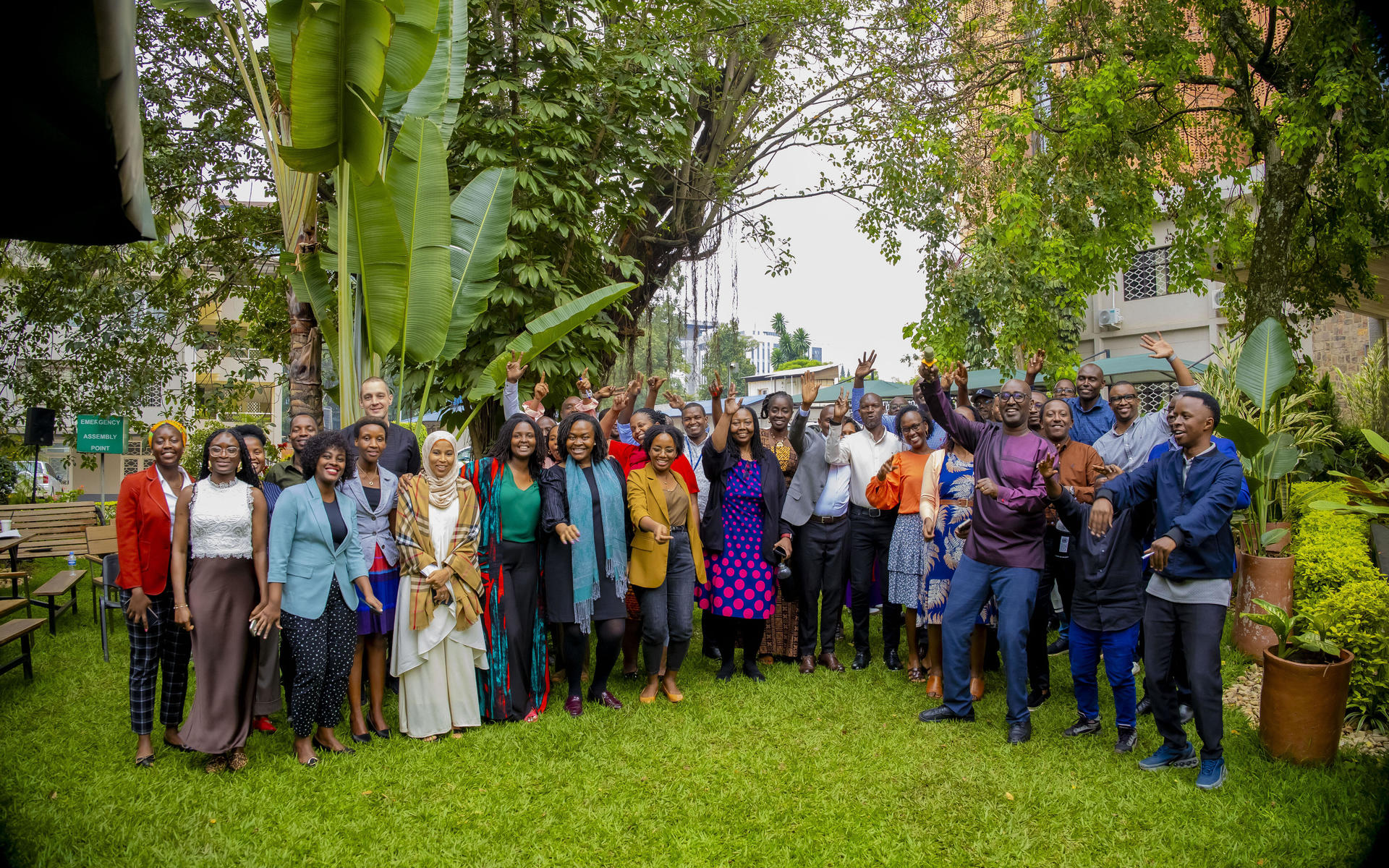 Large diverse group posing for a photo in a sunny garden with trees.