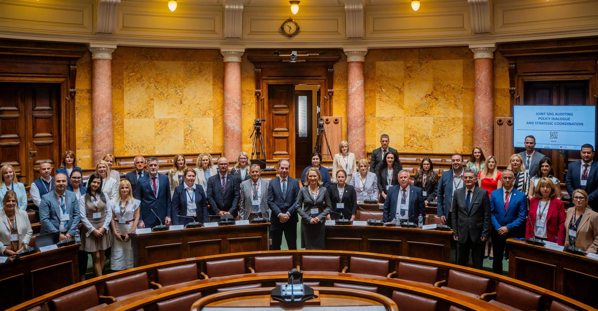 Group of suited officials posing in a grand wood-paneled council chamber.