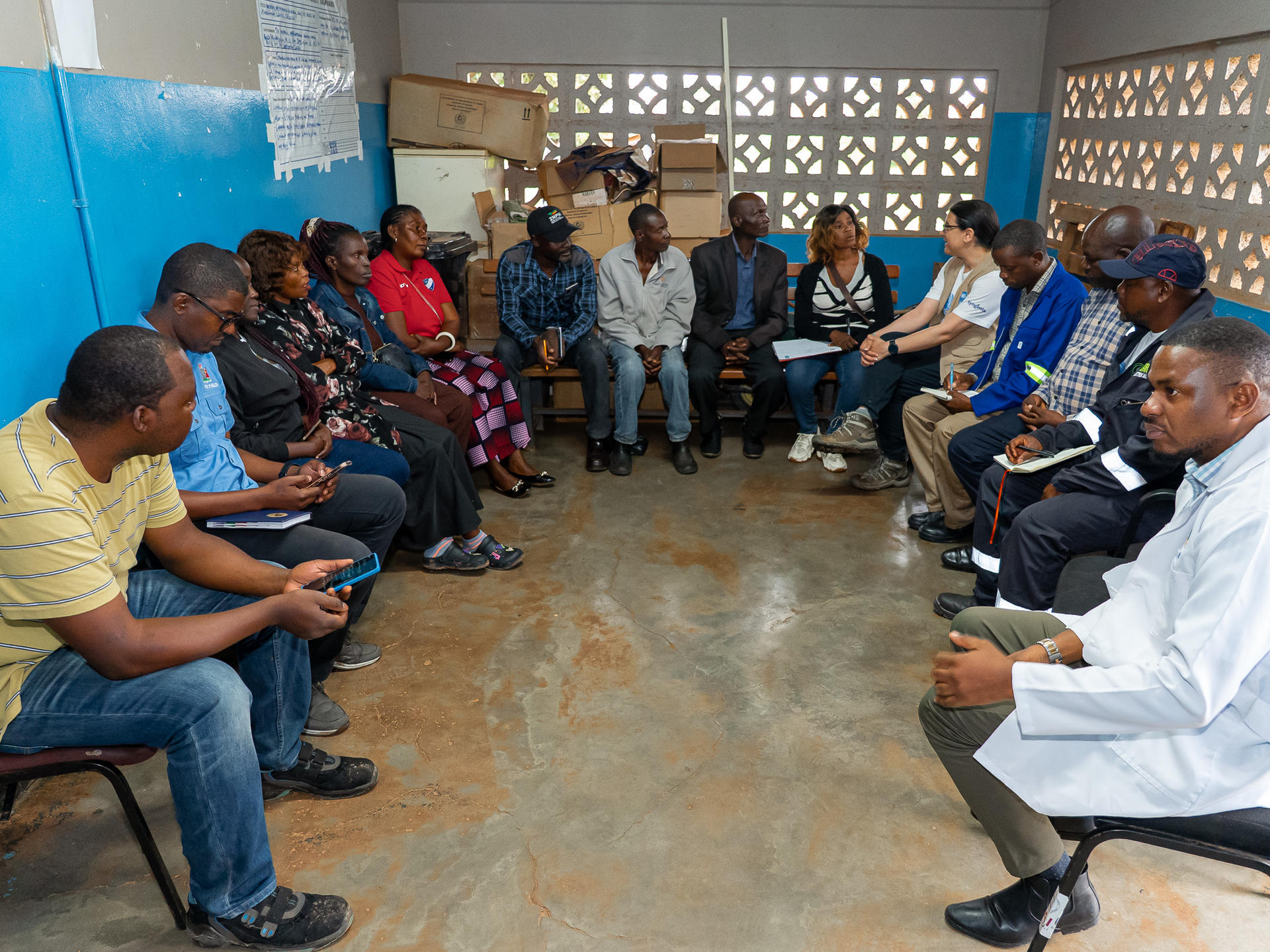 Photograph of a community meeting: people seated in a circle in a blue-walled room.