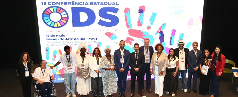 Photo: group of people on stage posing at a conference with a large ODS 2030 logo on screen.
