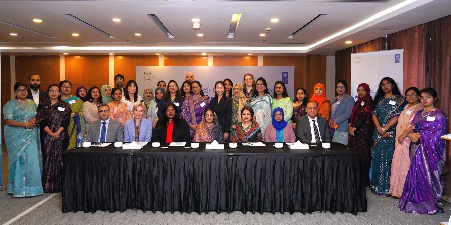 Group photograph of professionals in colorful attire standing behind a long table at a conference.