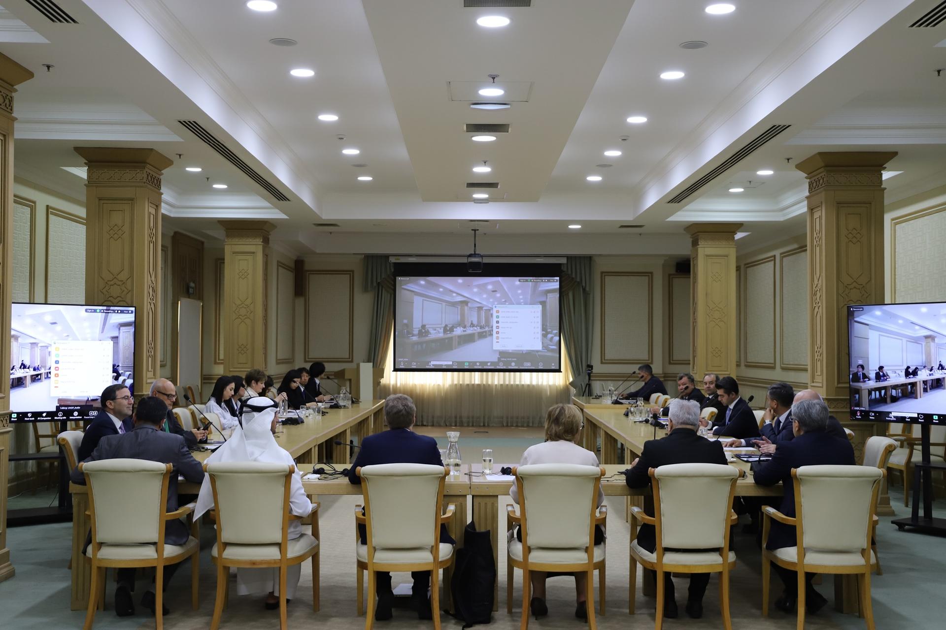 Photograph of a formal boardroom meeting with people around a long table and a front projector.