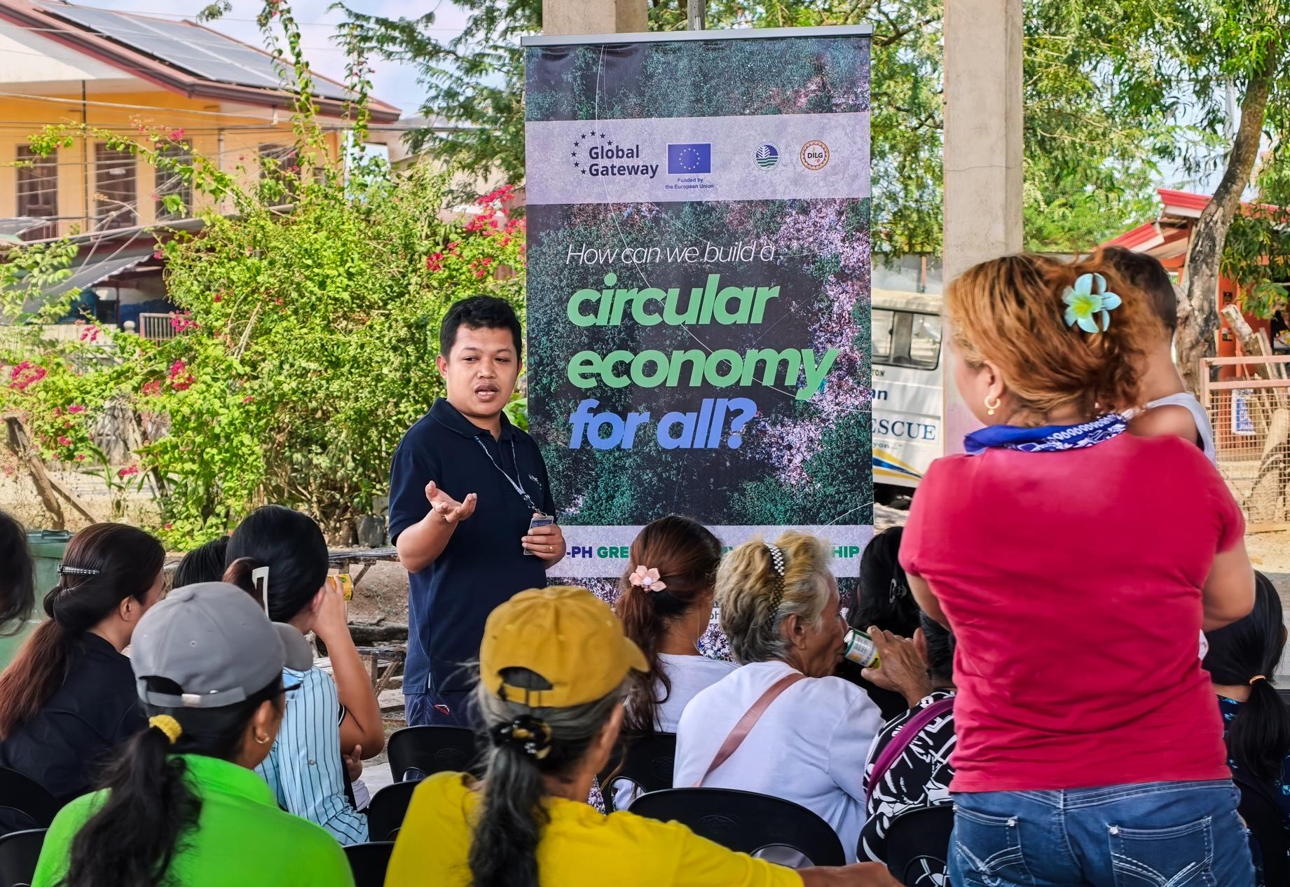 Photo: outdoor community event with a speaker and a banner that reads circular economy for all.