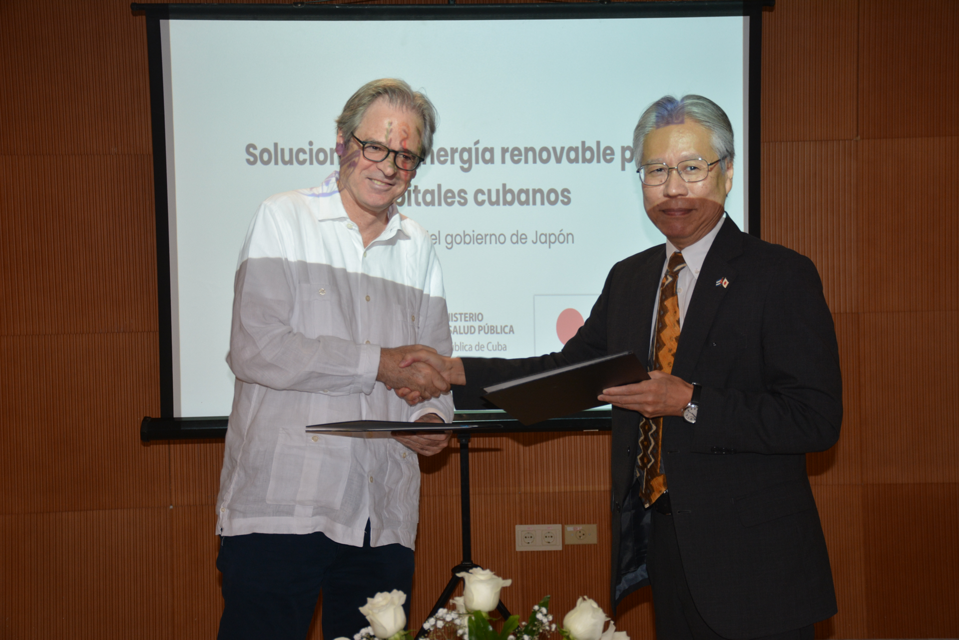 Photograph of two men on stage exchanging a certificate, with a projection screen behind.