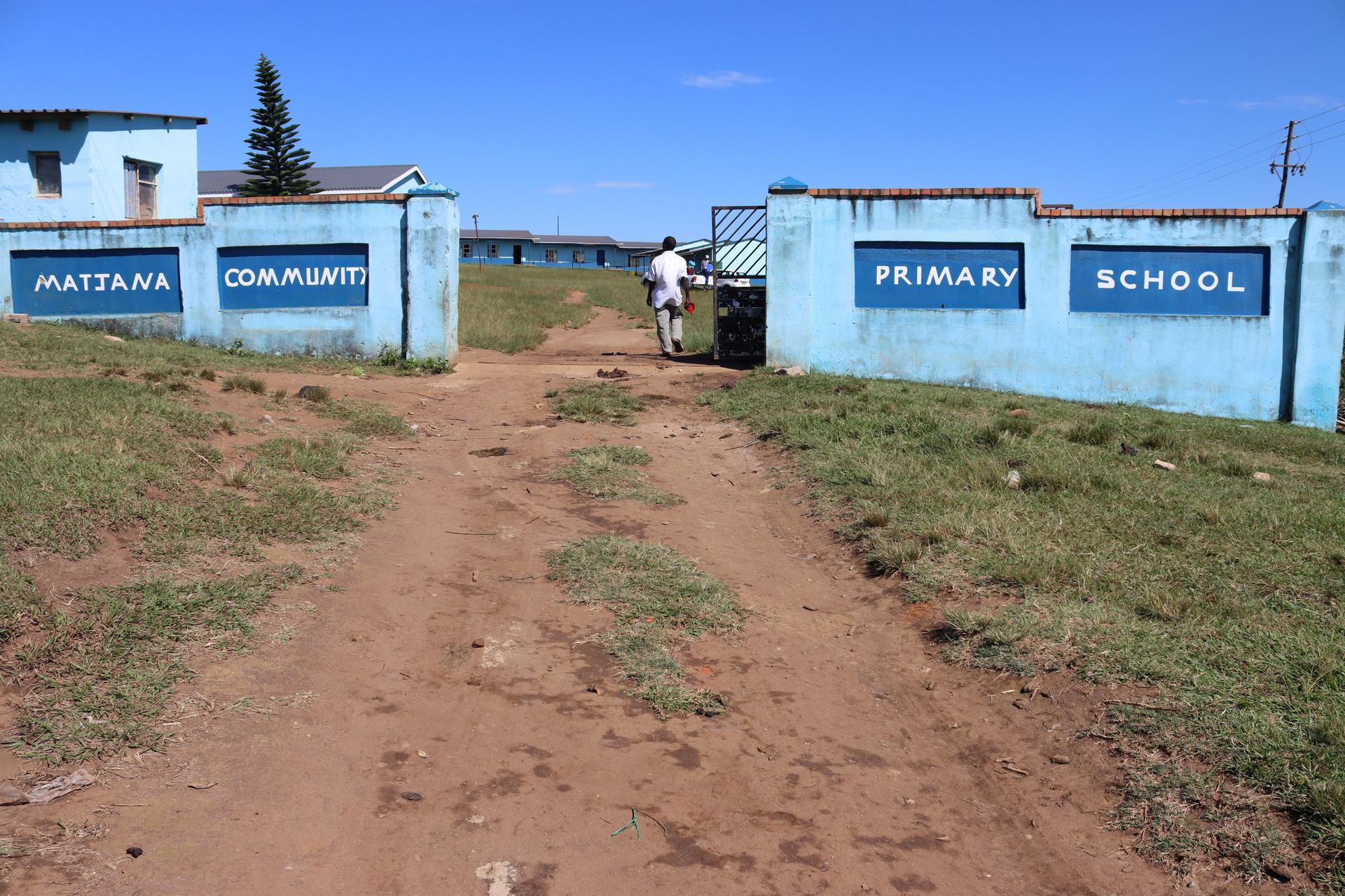 Dusty path between blue school blocks with signs reading Primary School under a clear blue sky.