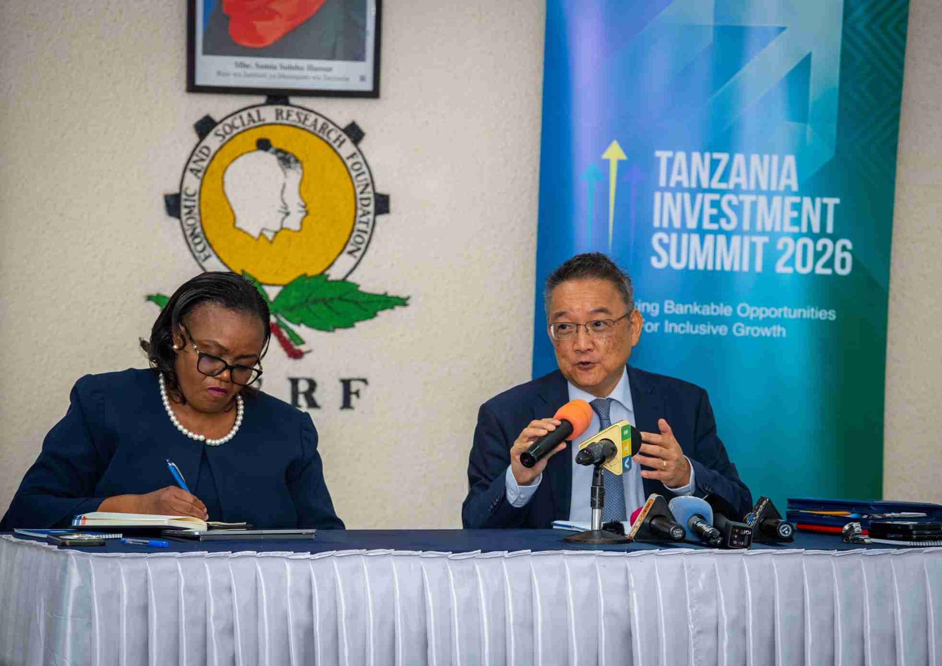 Photograph of two men at a Tanzania Investment Summit panel, one taking notes, the other speaking.