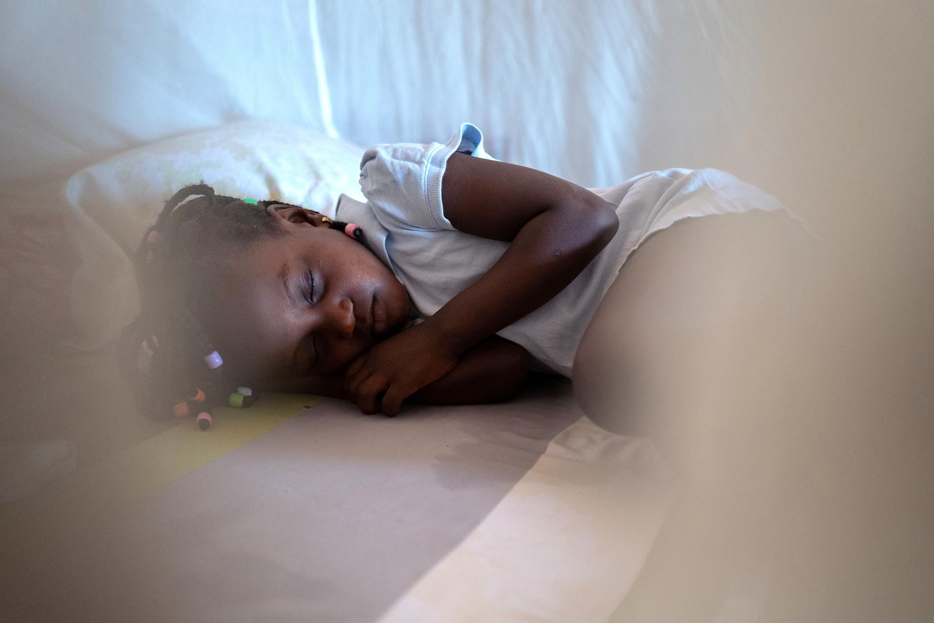 Photograph of a person sleeping on a bed with white sheets, head on a pillow, soft lighting.