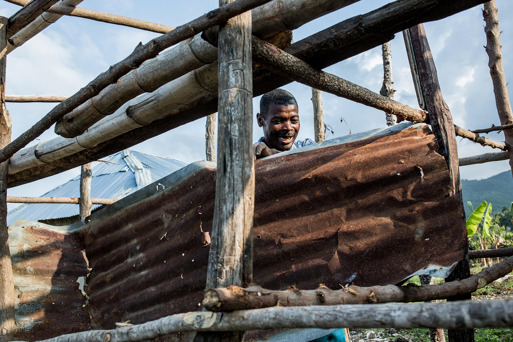 Smiling man peeks from a rustic log cabin under construction.