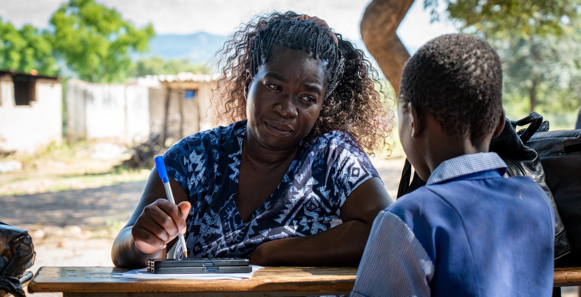 Photograph of two children studying at a desk outdoors; one face is blurred.
