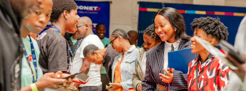 Group of people gathered around a booth at a busy event, smiling and talking.