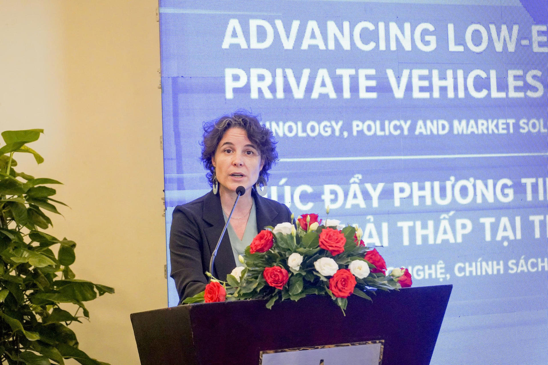 Speaker at podium with flower bouquet; blue slide about advancing private vehicles.