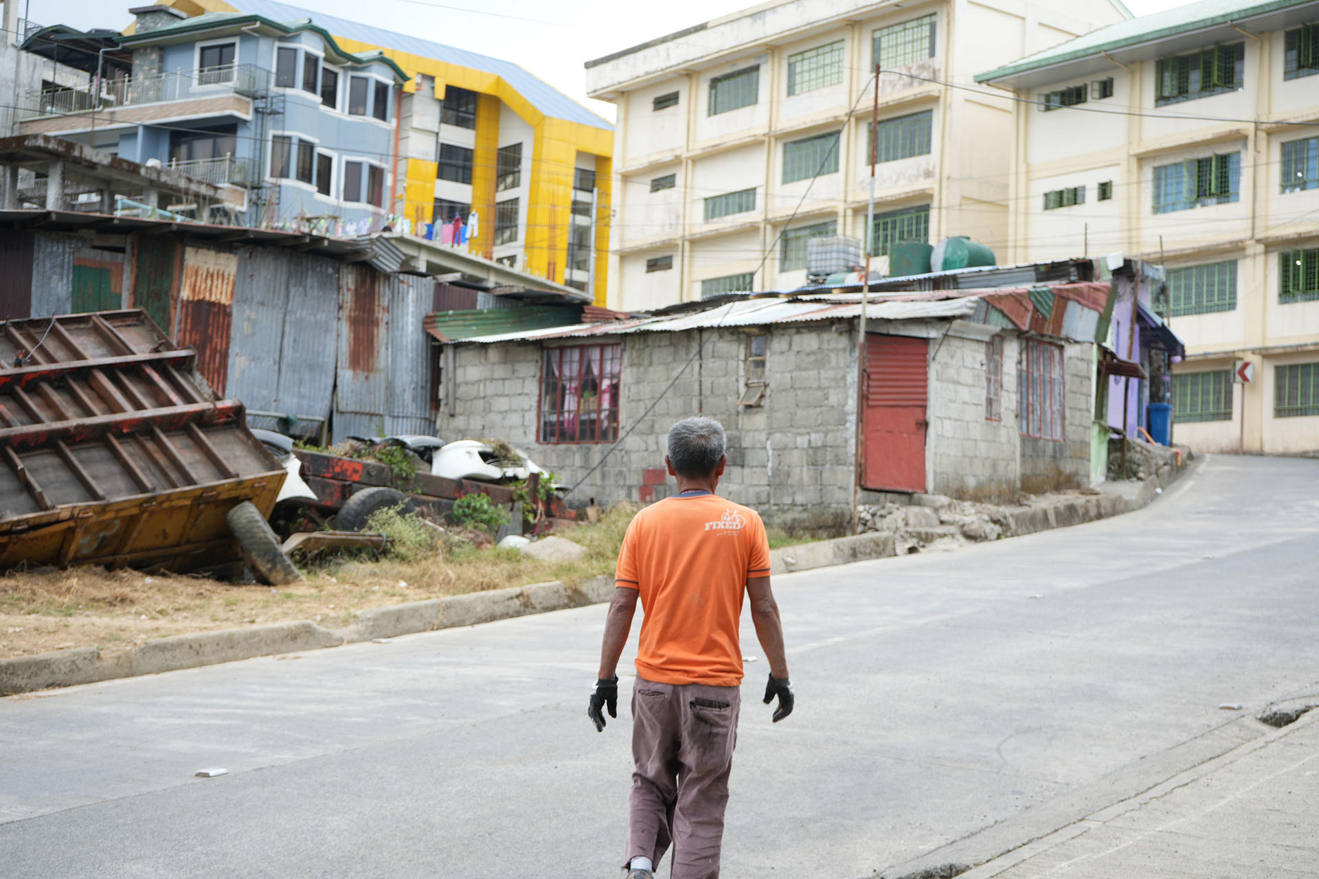 Man in orange shirt walking down a curved street with colorful buildings and rubble on the sides.