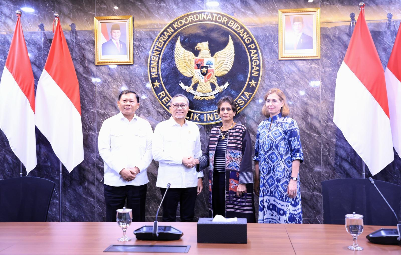 Four people pose in a formal meeting room with Indonesian flags and the national emblem.