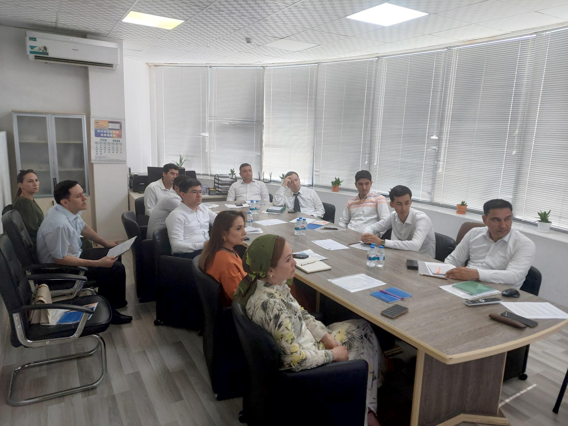 Group of people seated around a conference table in a bright office meeting room.