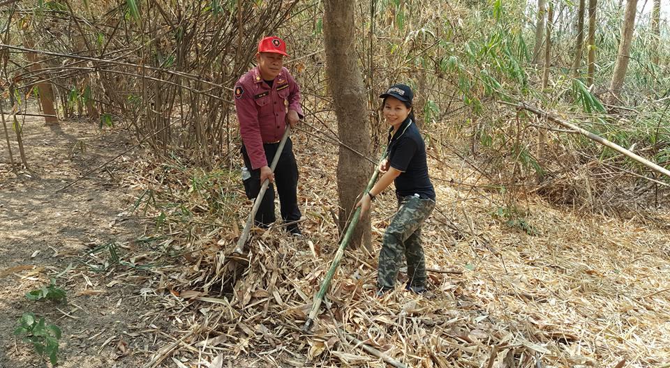 Two men with long-handled hoes work in a dry, leaf-covered forest clearing.