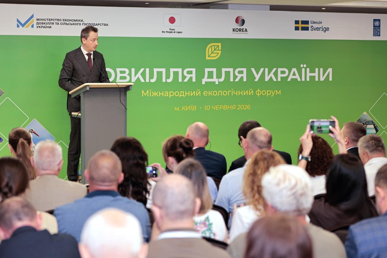 Male presenter at a podium addressing a conference; green banner background with Ukrainian text.