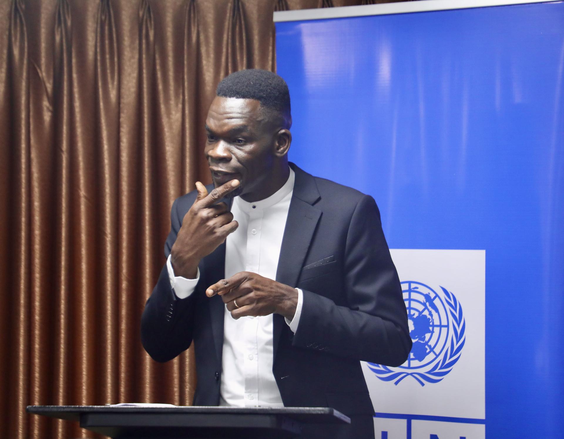 Man in a suit at a podium, with a blue United Nations banner in the background.