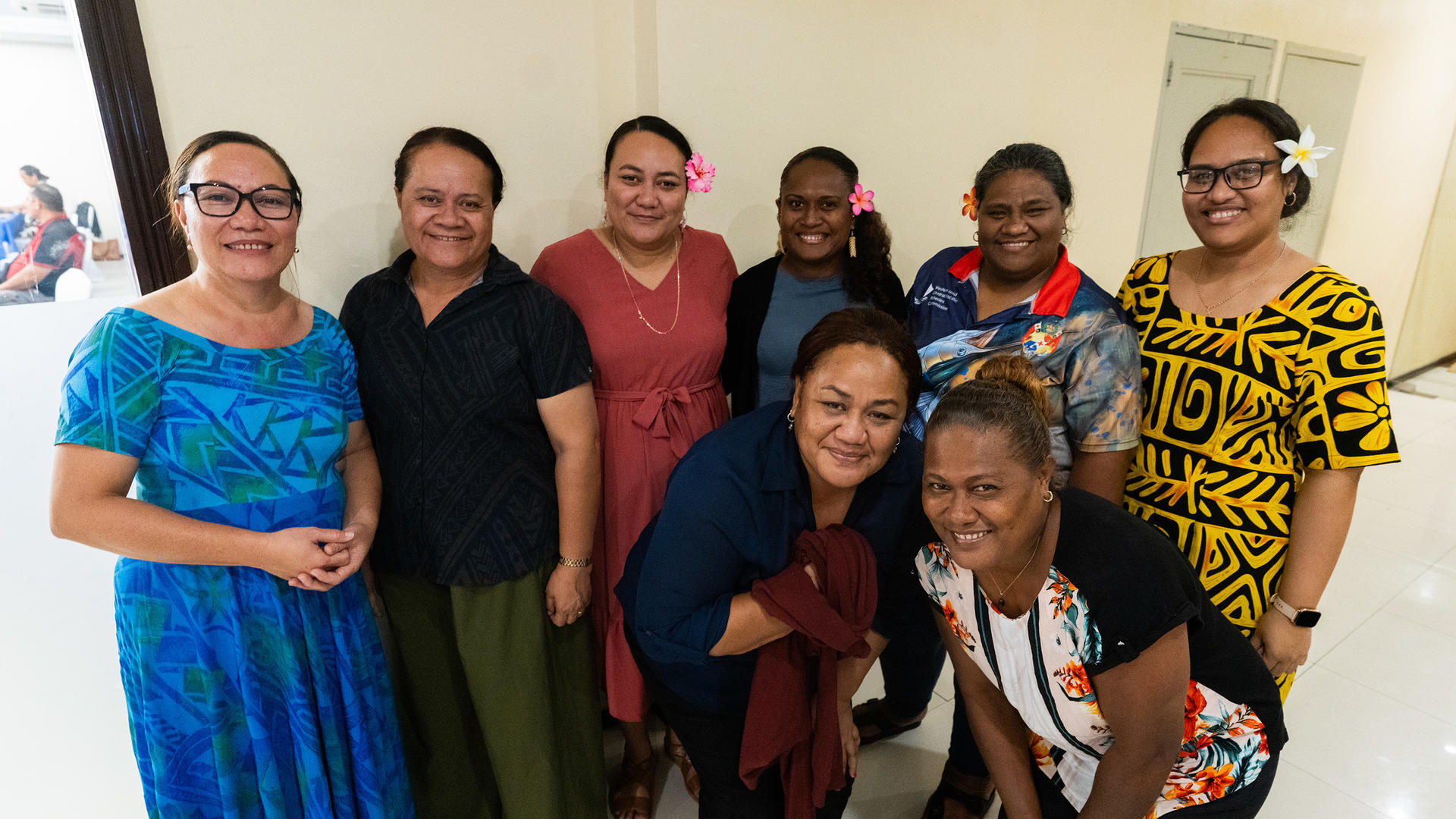Group of diverse adults posing and smiling in a bright indoor hallway.