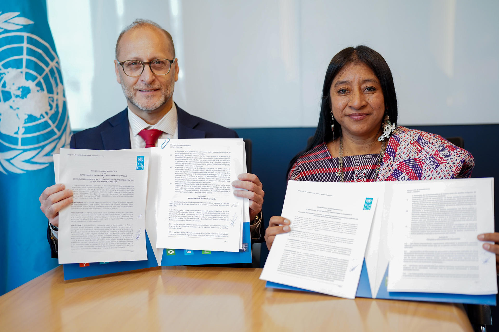 Two people signing documents at a UN event; faces blurred.