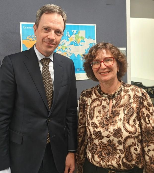 Two people pose; man in suit, woman in patterned blouse, blurred faces, world map.