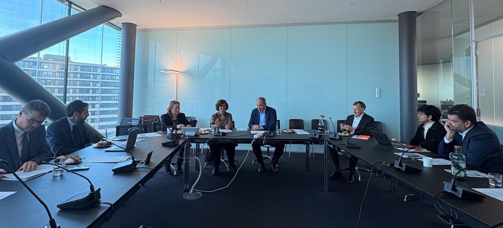 People in business attire sit around a long conference table in a blue-walled modern office.