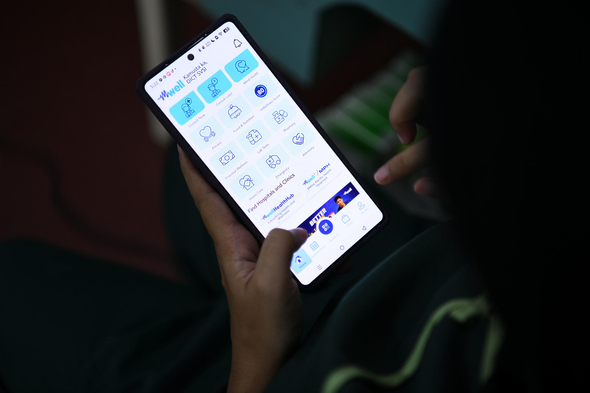 Photo: person holding a smartphone with app icons visible on the screen in a dim setting.