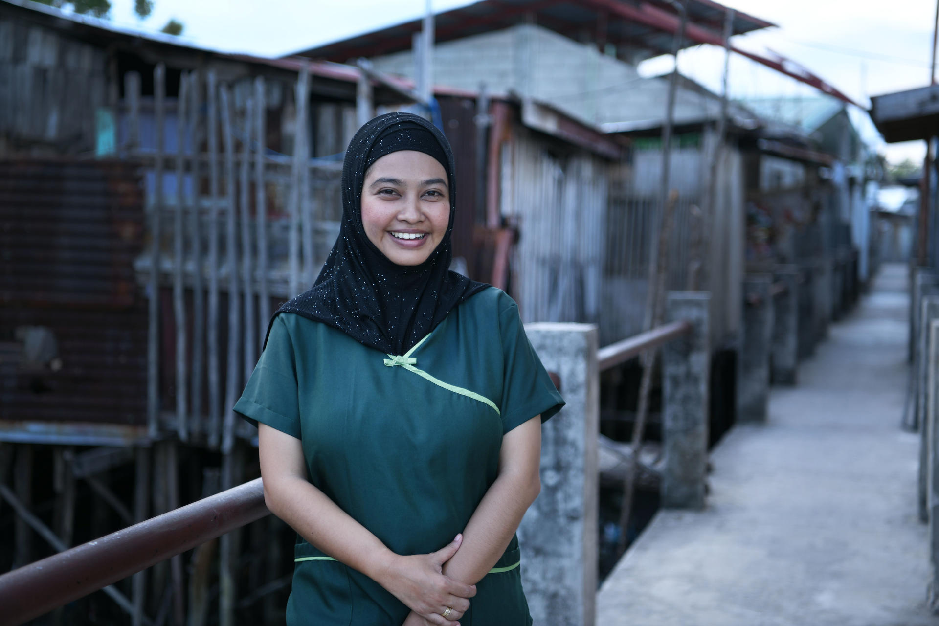 Photograph of a smiling woman in a green shirt and hijab, beside rows of bird cages.