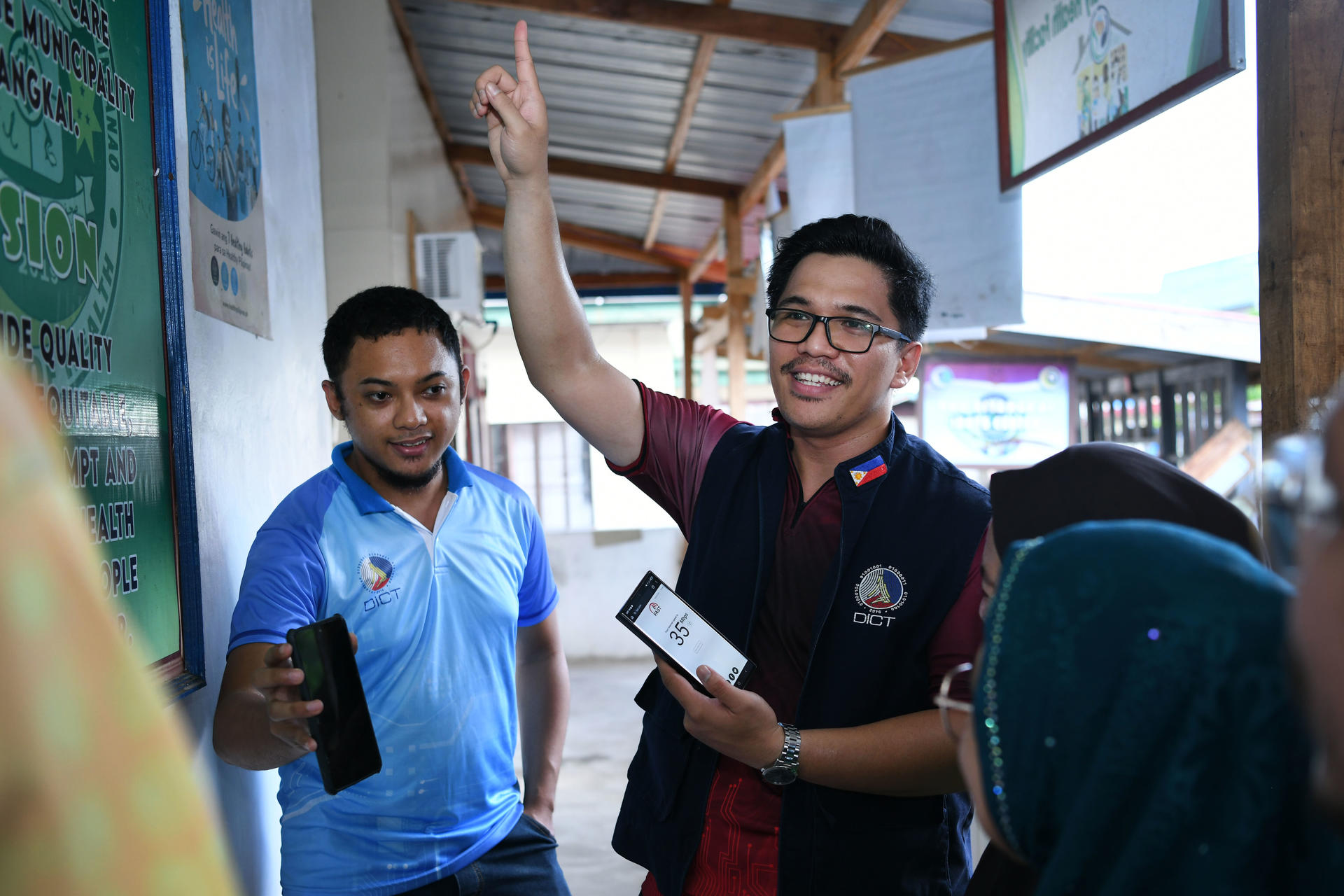 Smiling group in a hallway; man in maroon jacket and glasses raises his hand while holding tablet
