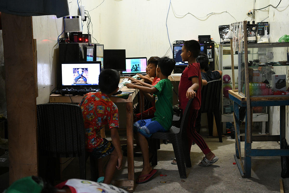 Group of children gathered around a computer at a cluttered workshop.