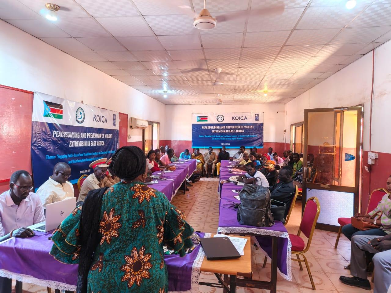 Training workshop in a community hall with attendees at tables and banners on the back wall.