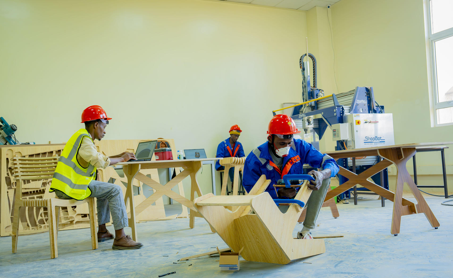 Children in safety vests and hard hats build a wooden project at a classroom workshop.
