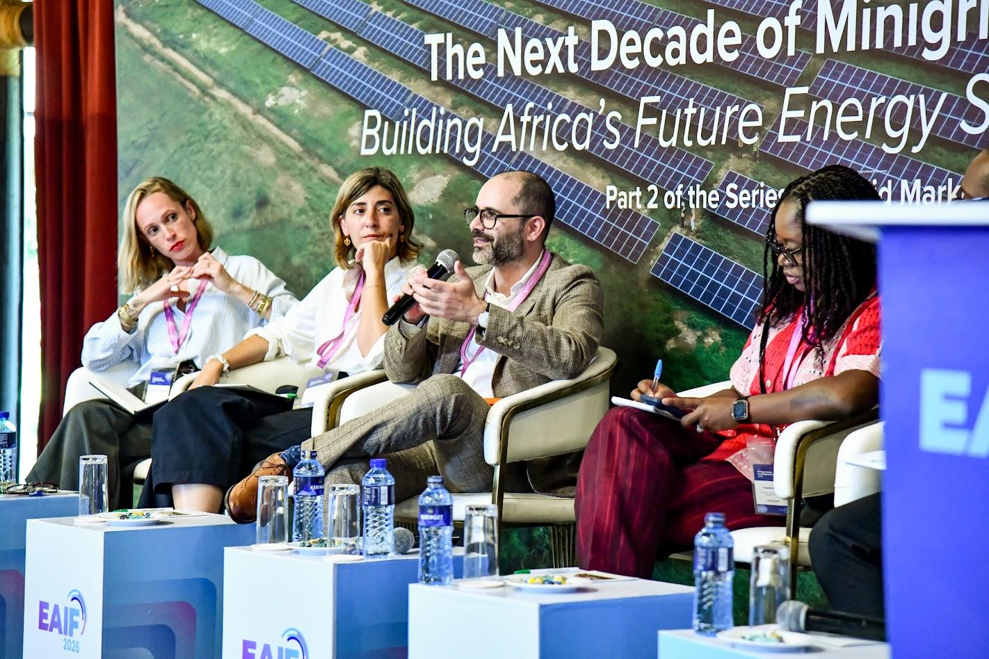 Photo: panel of speakers seated on stage at a conference with a banner in the background.