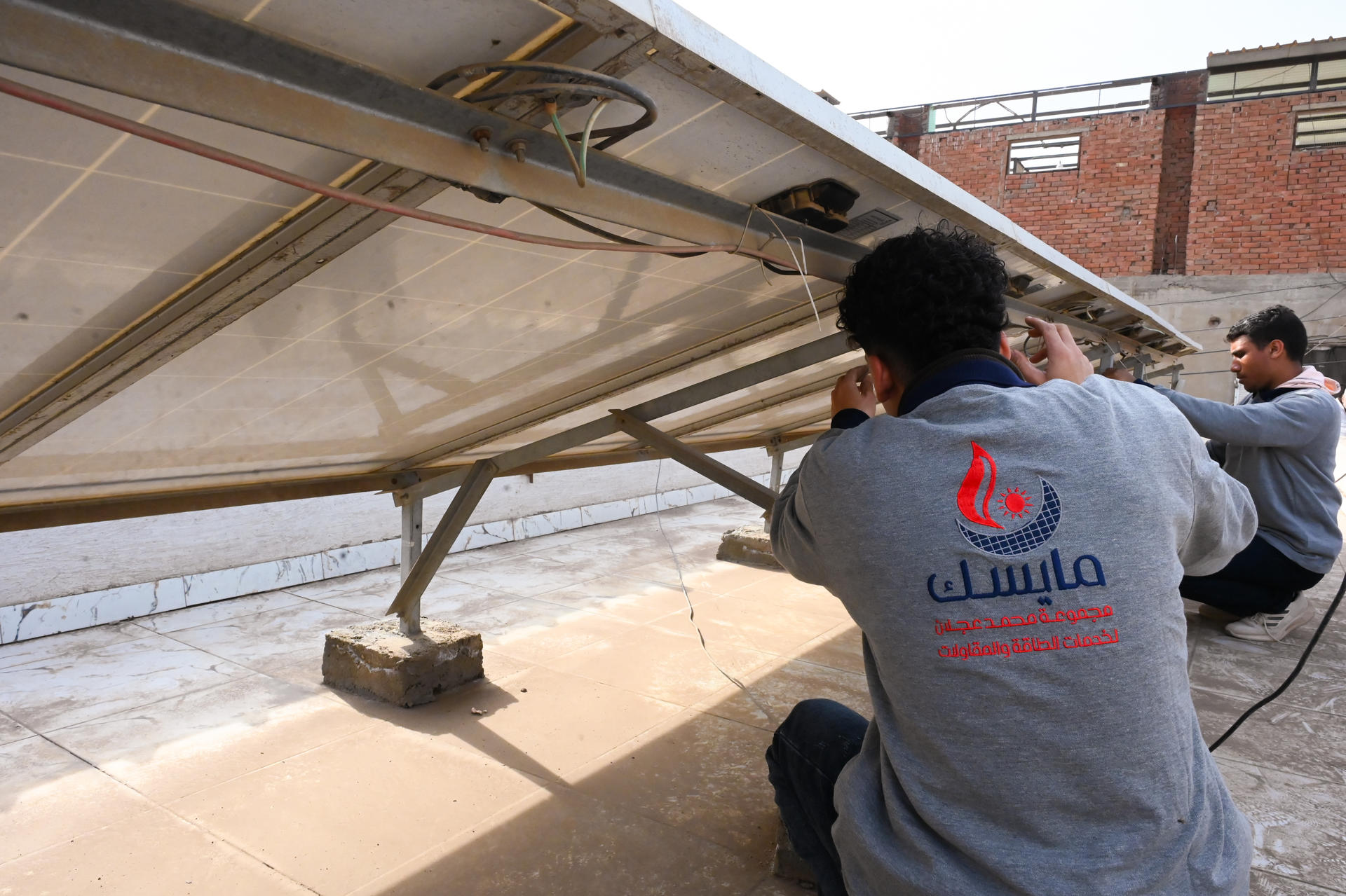 Three men in matching gray shirts work on a fabric-covered aircraft wing outdoors.