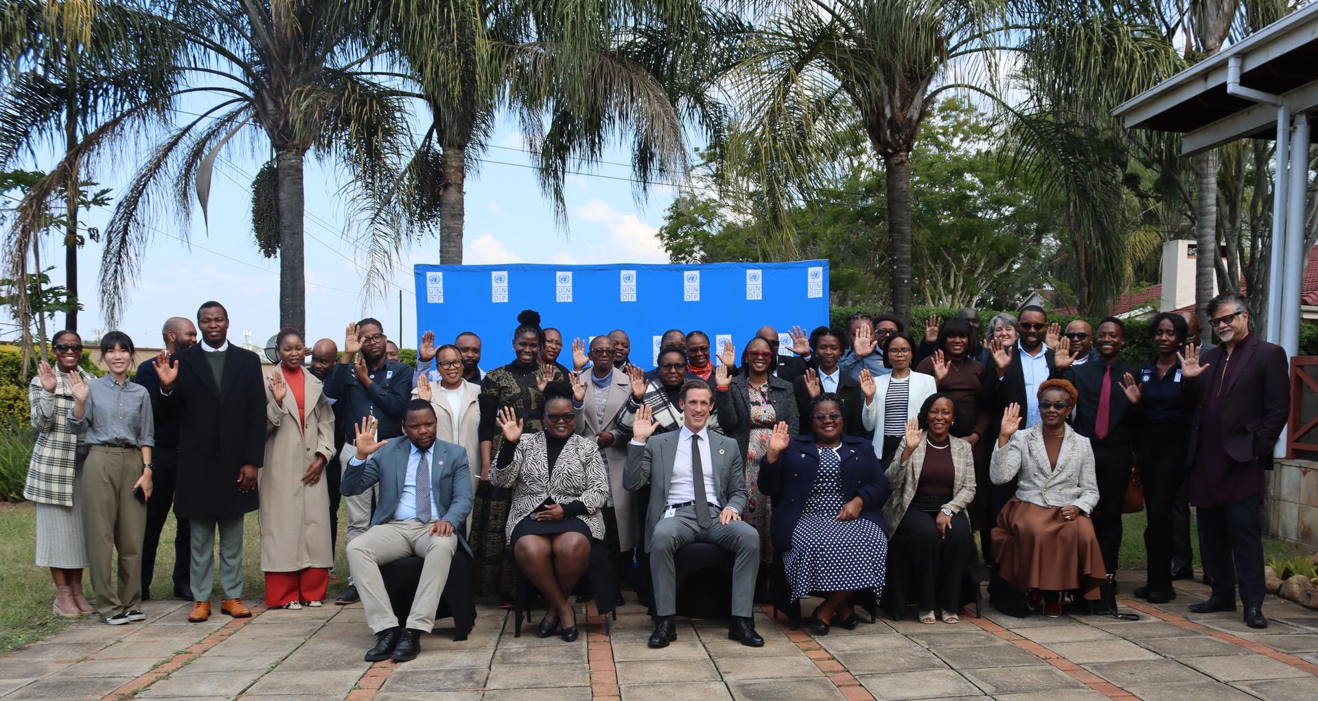Group of people posing outdoors in front of a blue backdrop with palm trees.