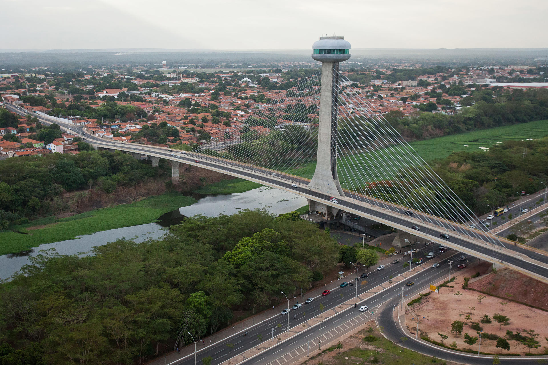 Photograph of a cityscape with a tall observation tower, a river bridge, and green spaces.