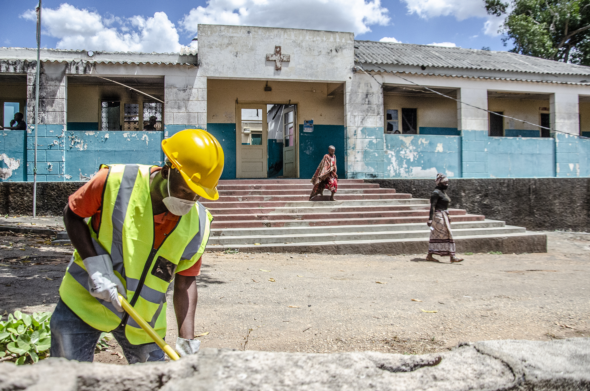 Construction worker in a yellow hard hat and reflective vest at a building site; child on steps behind.