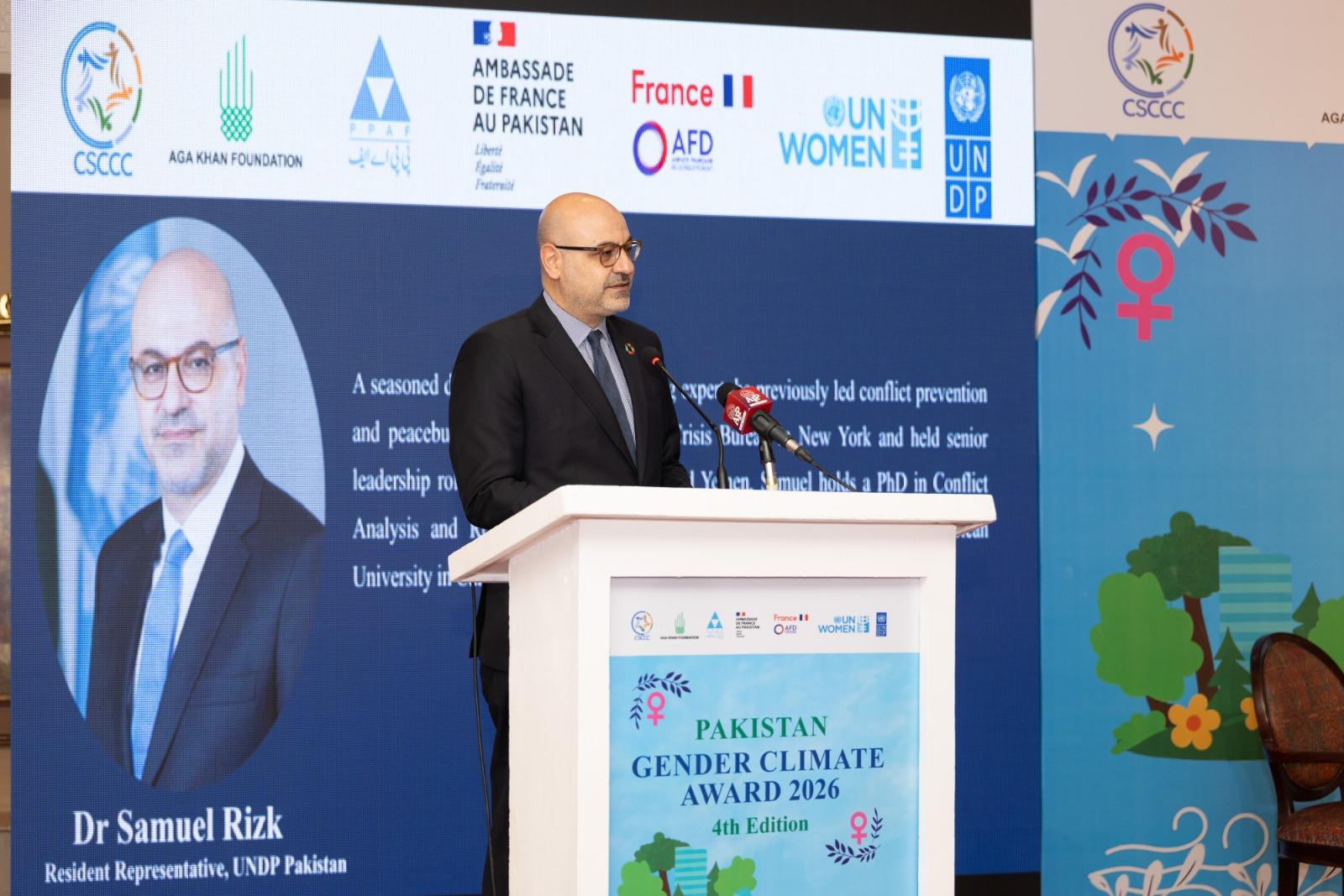 Photograph of a man in a suit speaking at a conference podium with blue banners.