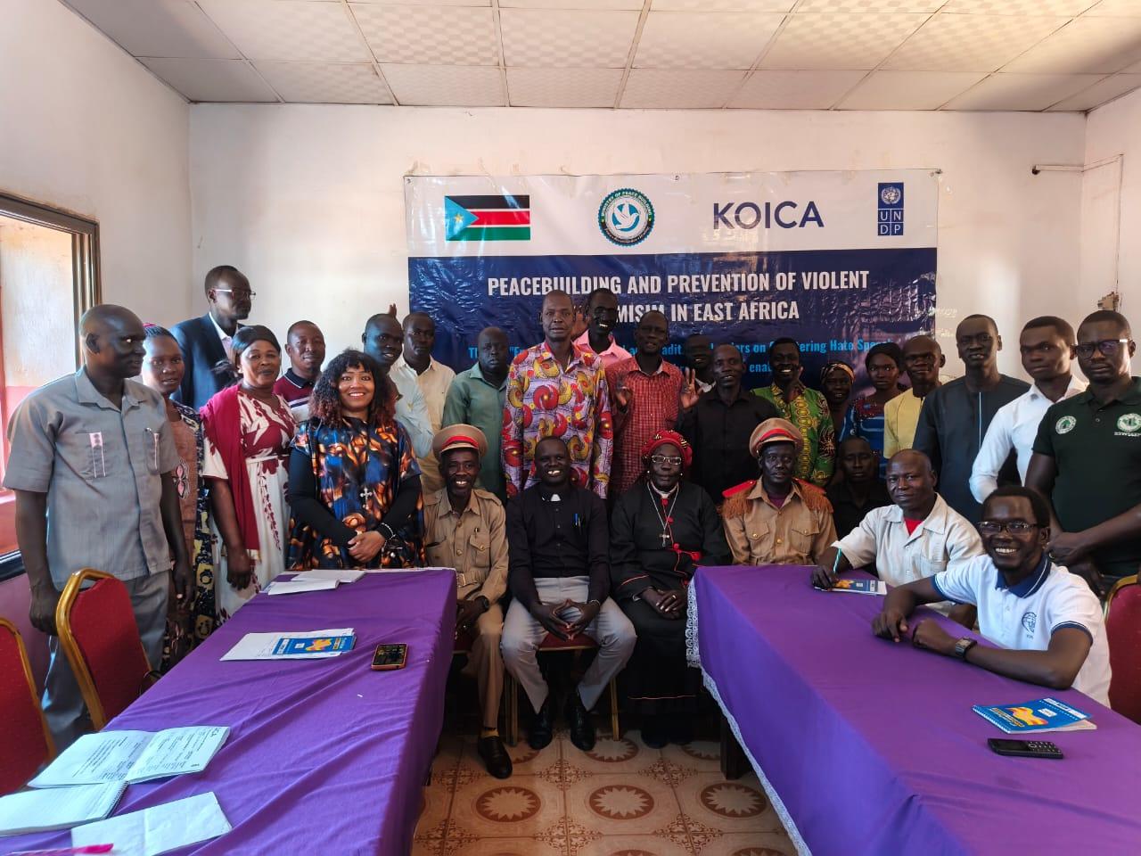 Group of people at a training workshop, purple tables in foreground, KOICA banner in background.